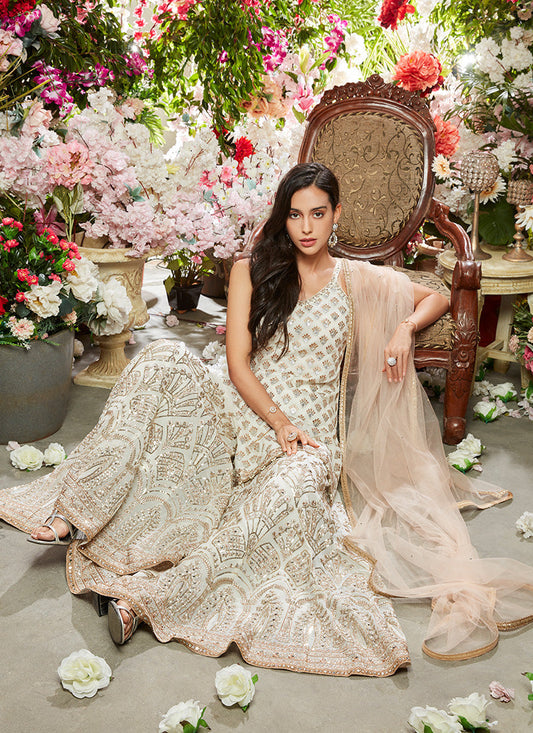 Indian woman fashioned in White and Gold Sharara Suit surrounded my colorful flowers